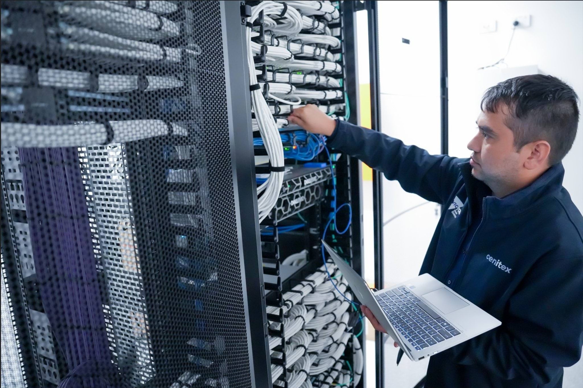 Man with laptop standing in front of server stack